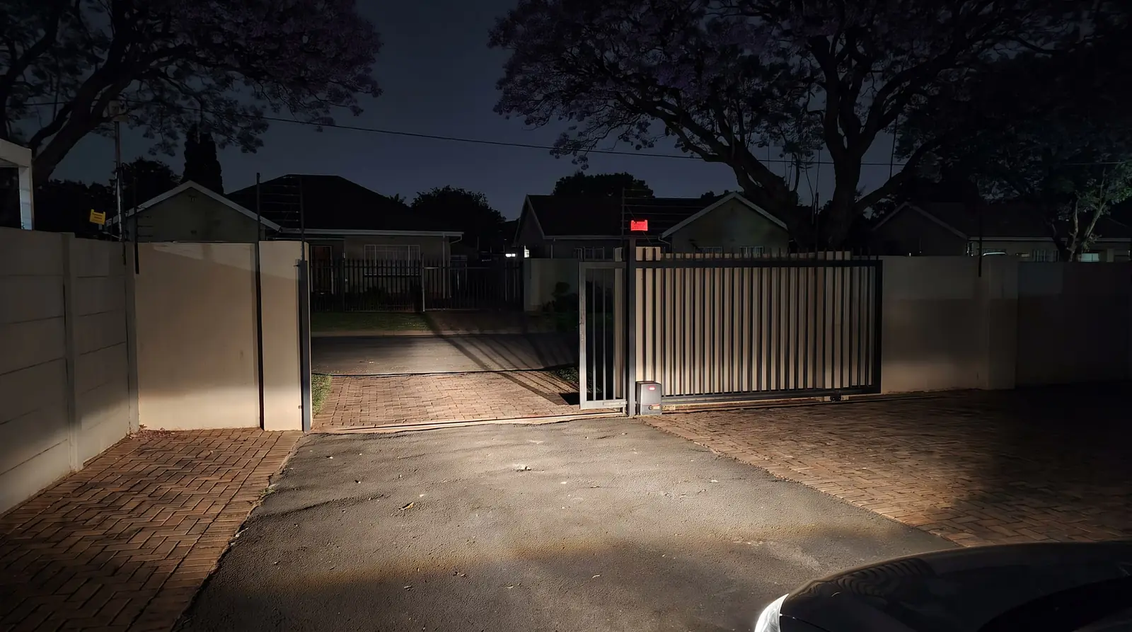 A driveway at night during a power cut, a sliding gate open and the houses around it dark